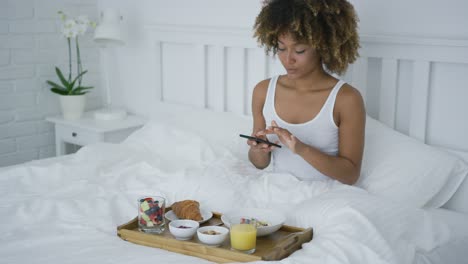 Charming-woman-using-phone-while-having-breakfast