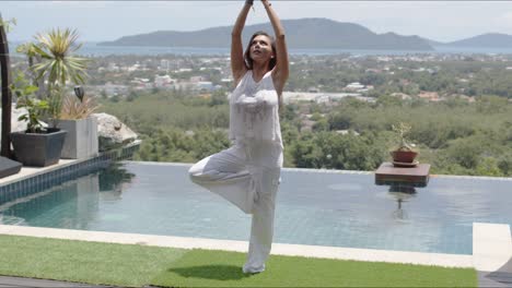 Mujer-Tranquila-Practicando-Yoga-Junto-A-La-Piscina-Contra-El-Hermoso-Paisaje-De-La-Orilla-Del-Mar
