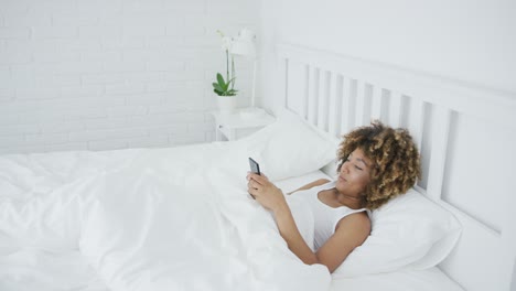 Smiling-woman-relaxing-with-phone-in-bed
