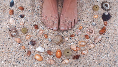 Woman-feet-on-the-sand-with-sea-shells