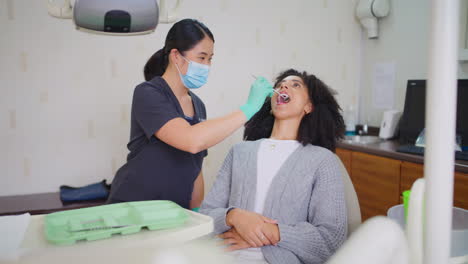 Dentist-with-face-mask-checking-teeth-of-female