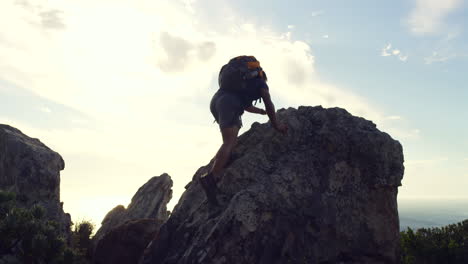 Man-reaching-the-top-of-a-mountain-against-sunset