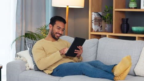 Young-man-happily-laying-on-couch-with-tablet