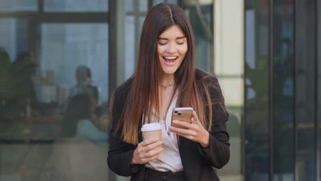 Smiling-young-female-banker-using-a-phone-outside
