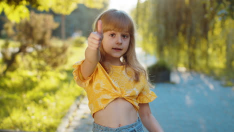 Happy-child-girl-showing-thumbs-up,-like-ok-yes-sign-good-positive-feedback-victory-win-in-city-park