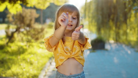 Happy-child-girl-showing-thumbs-up,-like-ok-yes-sign-good-positive-feedback-victory-win-in-city-park