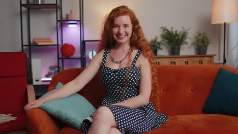 Redhead-girl-smiling-friendly-at-camera,-waving-hands-gesturing-hello,-hi,-greeting-at-home-on-couch