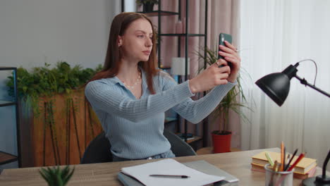 Young-woman-blogger-taking-selfie-portraits-on-smartphone-for-social-media-vlog-while-working-home