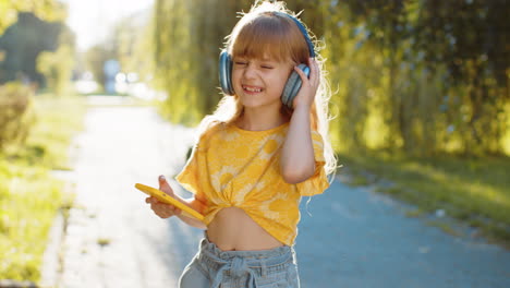 Niña-Feliz-Con-Auriculares-Inalámbricos-Eligiendo,-Escuchando-Música-En-Un-Teléfono-Inteligente-Bailando-Al-Aire-Libre