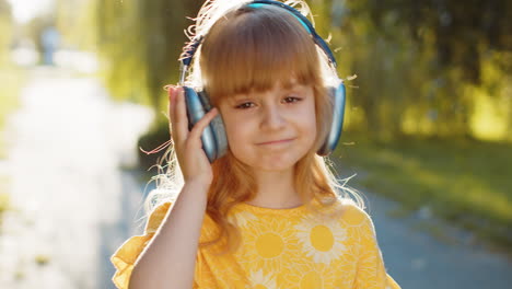 Happy-child-girl-in-wireless-headphones-choosing,-listening-music-in-smartphone-dancing-outdoors