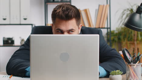 Confident-businessman-hiding-behind-laptop-computer,-looking-at-camera,-spying,-peeping