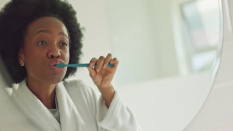 Black-woman-brushing-teeth-in-bathroom-mirror