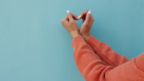 Woman-hands-with-heart-sign-against-wall-blue