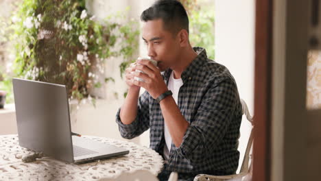 Man-drinking-coffee-while-working-on-a-laptop