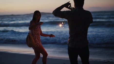 Fun-couple,-sparkles-and-phone-on-sunset-beach