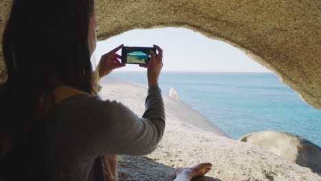 Beach,-cave-and-woman-with-phone-for-picture