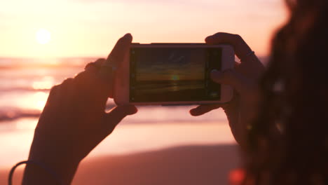 Hands,-phone-and-woman-at-the-beach-at-sunset