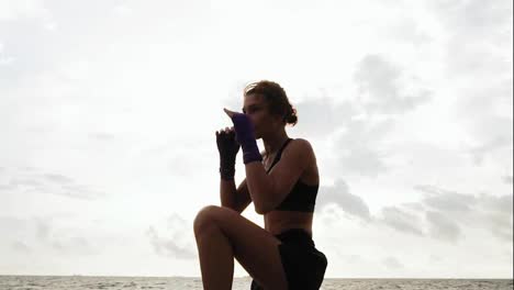 Tough-pretty-woman-shadowboxing.-Beautiful-female-boxer-training-by-the-sea-on-the-beach-in-the-morning,-throwing-punches-in