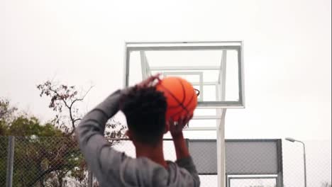 Back-view-of-unrecognizable-african-player-jumping-up-and-throwing-ball-in-a-basketball-hoop,-the-ball-hits-the-ring-and-scores