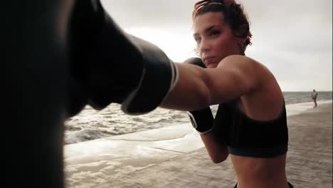 Nahaufnahme-Einer-Starken-Athletischen-Boxerin-In-Handschuhen,-Die-Mit-Einer-Tasche-Gegen-Den-Sohn-Am-Meer-Trainiert.-Boxertraining-Für-Frauen