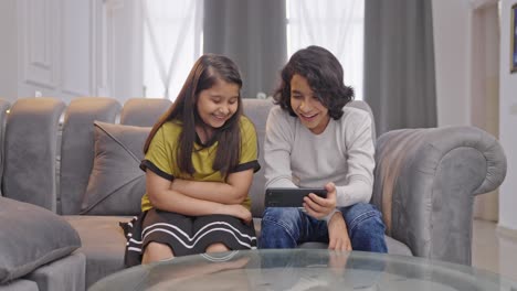 Happy-Indian-siblings-watching-video-in-mobile-phone-and-laughing