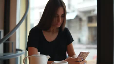 Attractive-young-lady-with-natural-makeup-using-her-mobile-phone-in-the-coffee-shot.-Modern-devices-usage.-Shopping-online