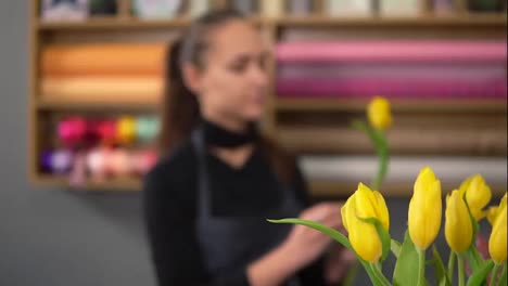 Junge-Attraktive-Lächelnde-Frau-In-Schürze,-Die-An-Blumenaufnahmen-Arbeitet-Und-Blumensträuße-Mit-Frischen-Gelben-Tulpen-Arrangiert