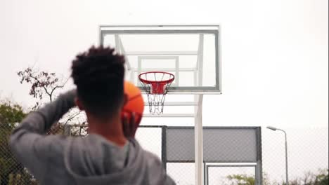 Young-african-player-jumping-up-and-throwing-ball-in-a-basketball-hoop,-the-ball-hits-the-ring-and-scores.-The-man-turns-around