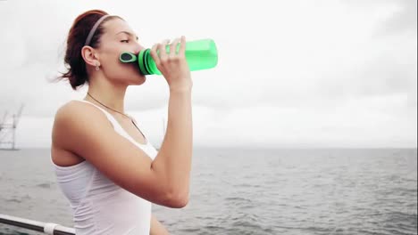 Durstige-Fitnessfrau,-Die-Sich-Nach-Dem-Training-Ausruht-Und-Eine-Wasserflasche-Trinkt.-Schöne-Frau-Beim-Training-Am-Meer