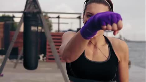 Close-Up-view-of-a-young-woman-training-with-her-hands-wrapped-in-purple-boxing-tapes-and-looking-in-the-camera.-Training-by-the