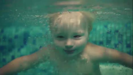 Cute-blonde-toddler-is-diving-under-the-water-in-the-swimming-pool-and-swimming-there-until-his-mother-helps-him-to-get-out.-and