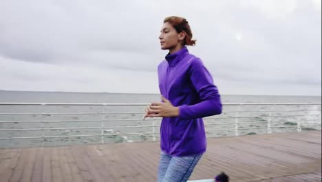 Close-up-view-of-young-athletic-woman-running-outdoors-in-slow-motion-on-promenade-near-ocean-enjoying-early-morning-run