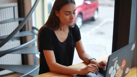 Young-woman-sitting-in-the-coffee-shot-by-the-window-with-her-laptop-and-thinking-what-to-write-or-how-to-answer.-Then-she-has