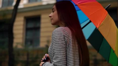 Close-Up-view-of-a-young-beautiful-woman-walking-and-spinning-her-colorful-umbrella-in-a-rainy-day-in-the-city-streets