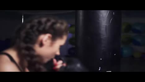 Young-woman-in-boxing-gloves-training-with-a-punching-bag-in-a-boxing-club.-Slow-Motion-shot