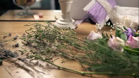Slow-camera-movement-showing-wooden-table-with-flowers,-scissors,-tapes,-decorating-paper-and-other-tools-for-bouquet