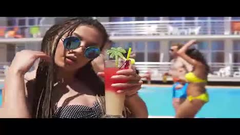 Young-beautiful-girl-with-dreads-and-sunglasses-coming-closer-to-camera-while-dancing-on-the-pool-party.-Summertime-Slow-Motion