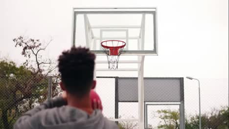 Back-view-of-unrecognizable-african-player-throwing-ball-in-a-basketball-hoop,-the-ball-hits-the-ring-and-scores.-Slow-Motion