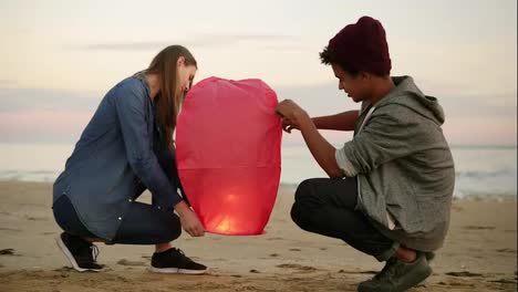 Cute-multi-ethnic-couple-holding-red-paper-lantern-before-launching.-Attractive-woman-with-her-african-boyfriend-holding-lantern