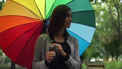 Portrait-of-a-young-beautiful-happy-woman-walking-and-spinning-her-colorful-umbrella-in-a-rainy-day-in-the-city-park