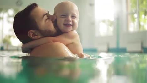 Cute-little-baby-and-his-father-having-swimming-lesson-in-the-pool.-The-father-is-holding-his-son-in-his-hands-and-embracing-him
