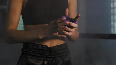 Close-Up-view-of-female-hands-being-wrapped-for-boxing-in-dark-room-with-smoke.-Young-fit-woman-wrapping-hands-with-purple-boxing
