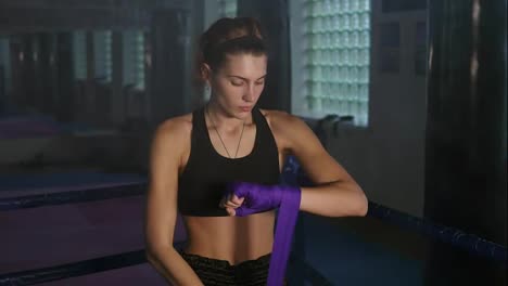 Muay-thai-female-boxer-wrapping-purple-bandages-on-her-hands-before-fight-in-dark-room-with-smoke