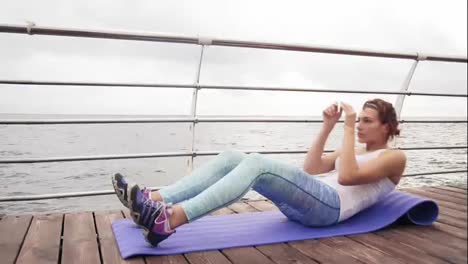 Young-athletic-woman-doing-situps-on-the-mat-and-boxing-doing-kicks-by-the-ocean-in-the-early-morning.-Fitness-woman-doing-abs