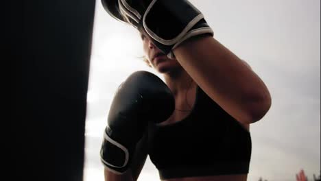 Close-Up-view-of-a-strong-athletic-female-boxer-in-gloves-exercising-with-a-bag.-Workout-outside.-Female-boxer-training.-Self