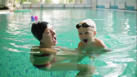 Happy-little-boy-is-swimming-in-the-pool-together-with-his-mother.-She-is-holding-him-and-teaching-how-to-swim.-Happy-family
