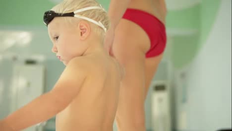 Back-view-of-young-mother-and-her-cute-little-blonde-child-walking-near-swimming-pool.-Happy-mom-spending-time-playing-with-her