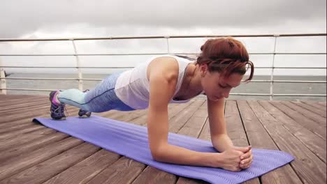 Round-camera-movement:-Young-woman-doing-elbow-plank-exercise.-Training-on-the-beach-in-front-of-the-ocean.-Morning-gymnastic