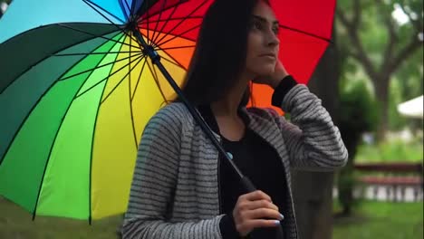 Retrato-De-Una-Joven-Hermosa-Mujer-Caminando-Con-Un-Paraguas-Colorido-En-Un-Día-Lluvioso-En-El-Parque-De-La-Ciudad