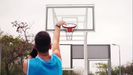 Back-view-of-unrecognizable-player-throwing-ball-in-a-basketball-hoop,-the-ball-hits-the-ring-and-scores.-Slow-Motion-shot